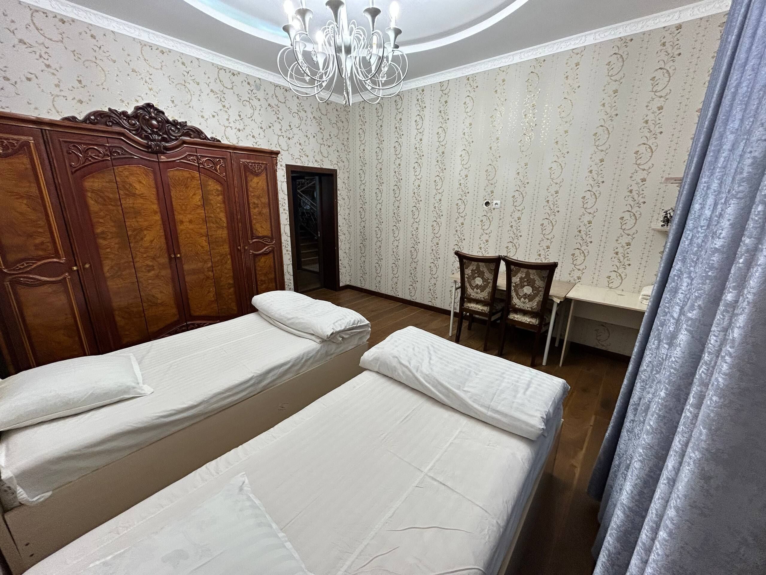 A room with two beds, a wooden wardrobe, a chandelier, and patterned wallpaper.