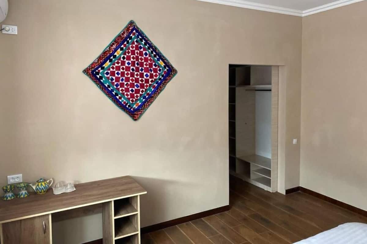 Una habitación con suelo de madera, un armario, una cama y un edredón de colores en la pared.