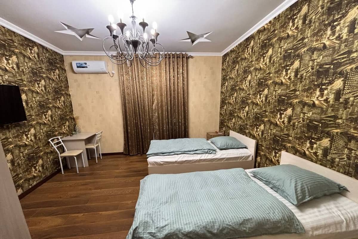 Una habitación con dos camas, un escritorio, una silla, una araña y papel tapiz estampado.