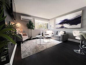 Ein modernes Wohnzimmer mit einem grauen Sofa, einem runden Couchtisch und einem großen, abstrakten Gemälde an der Wand.