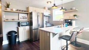 A modern kitchen with stainless steel appliances, wooden cabinets, and a bar area with stools.