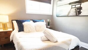 A neatly made bed with a white duvet, a wooden headboard, and a small bedside table with a lamp.