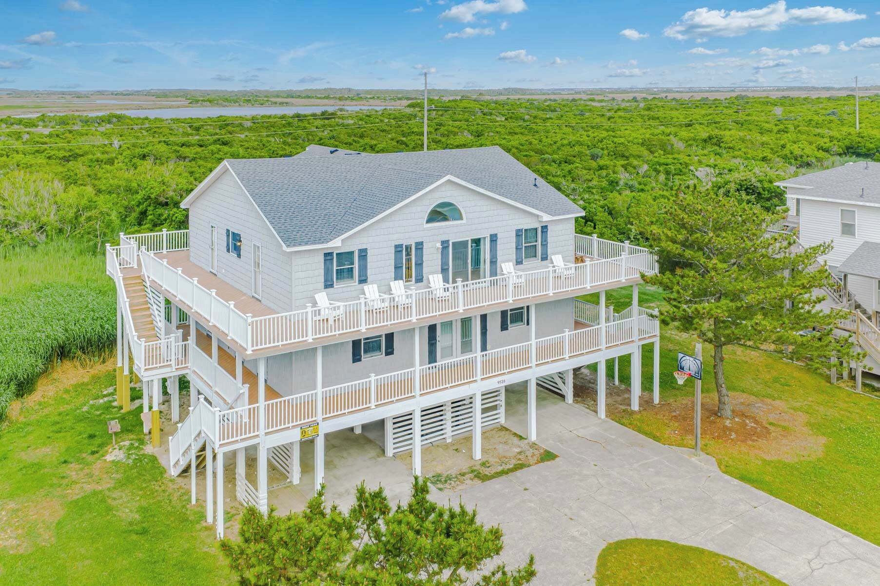 Une maison à deux étages située en bord de mer, dotée d’un balcon, d’un garage et d’un panier de basketball.