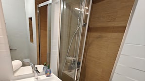 Ein modernes Badezimmer mit einer Duschkabine, einem weißen Waschbecken und einer Holzkommode.