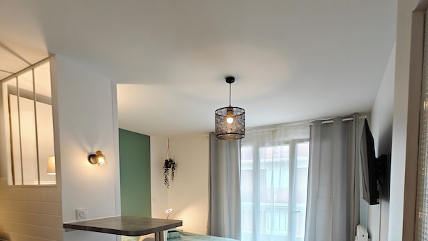 Ein kleines Zimmer mit einem Bett, einem Schreibtisch, zwei Stühlen, einer Pendelleuchte und einem Fernseher.