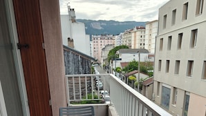 Ein Balkon mit Tisch und Stühlen, mit Blick auf eine Straße mit parkenden Autos und Gebäuden.