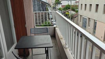 Un balcón con mesa y sillas, con vistas a una calle con coches aparcados y edificios.