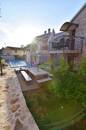 A pool area with a stone deck, outdoor furniture, and a stone building with a balcony. - Spacious Poolside Apartment in Tar (Tar-Vabriga)