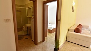 A hotel room with a bathroom, a bed, a white sofa, and a potted plant. - Spacious Poolside Apartment in Tar (Tar-Vabriga)