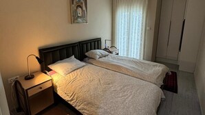 Ein Hotelzimmer mit zwei Betten, einem Nachttisch, einem Schreibtisch, einem Gemälde, einem Fenster mit Vorhängen und einem Kleiderschrank.