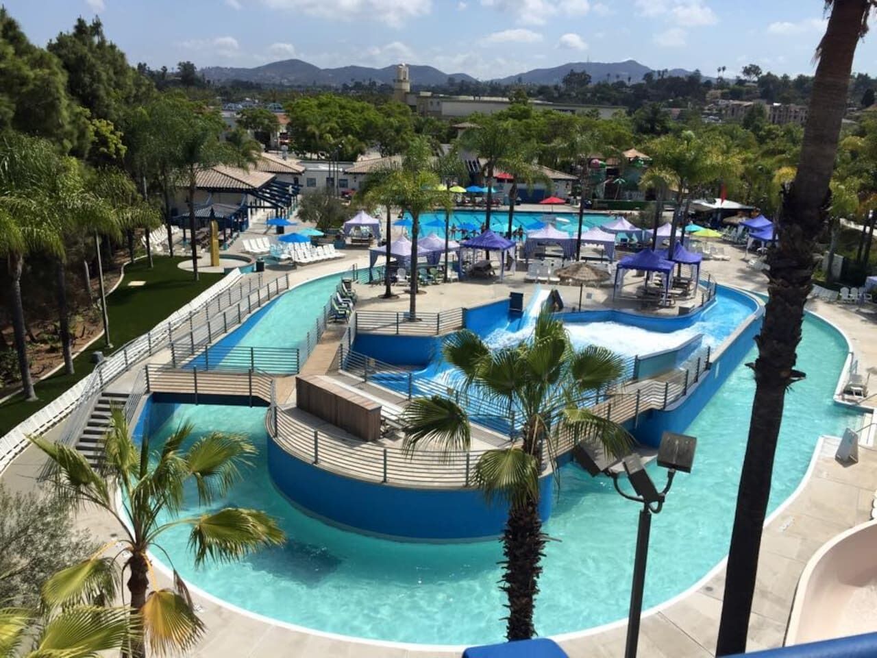 Una piscina con un tobogán central, rodeada de palmeras y sillas de descanso.