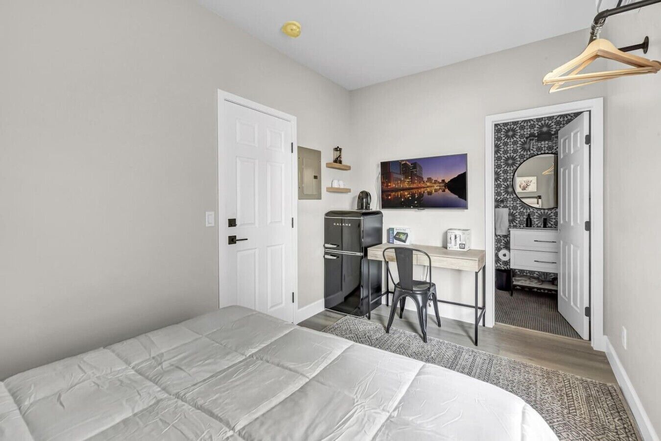 A bedroom with a bed, a desk, a chair, a wardrobe, and a bathroom visible through an open door.