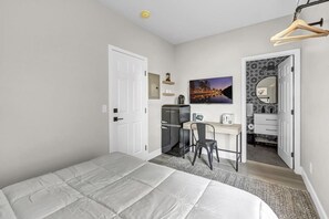 A bedroom with a bed, a desk, a chair, a wardrobe, and a bathroom visible through an open door.