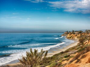A coastal landscape with a beach, ocean waves, and a cliff with houses.
