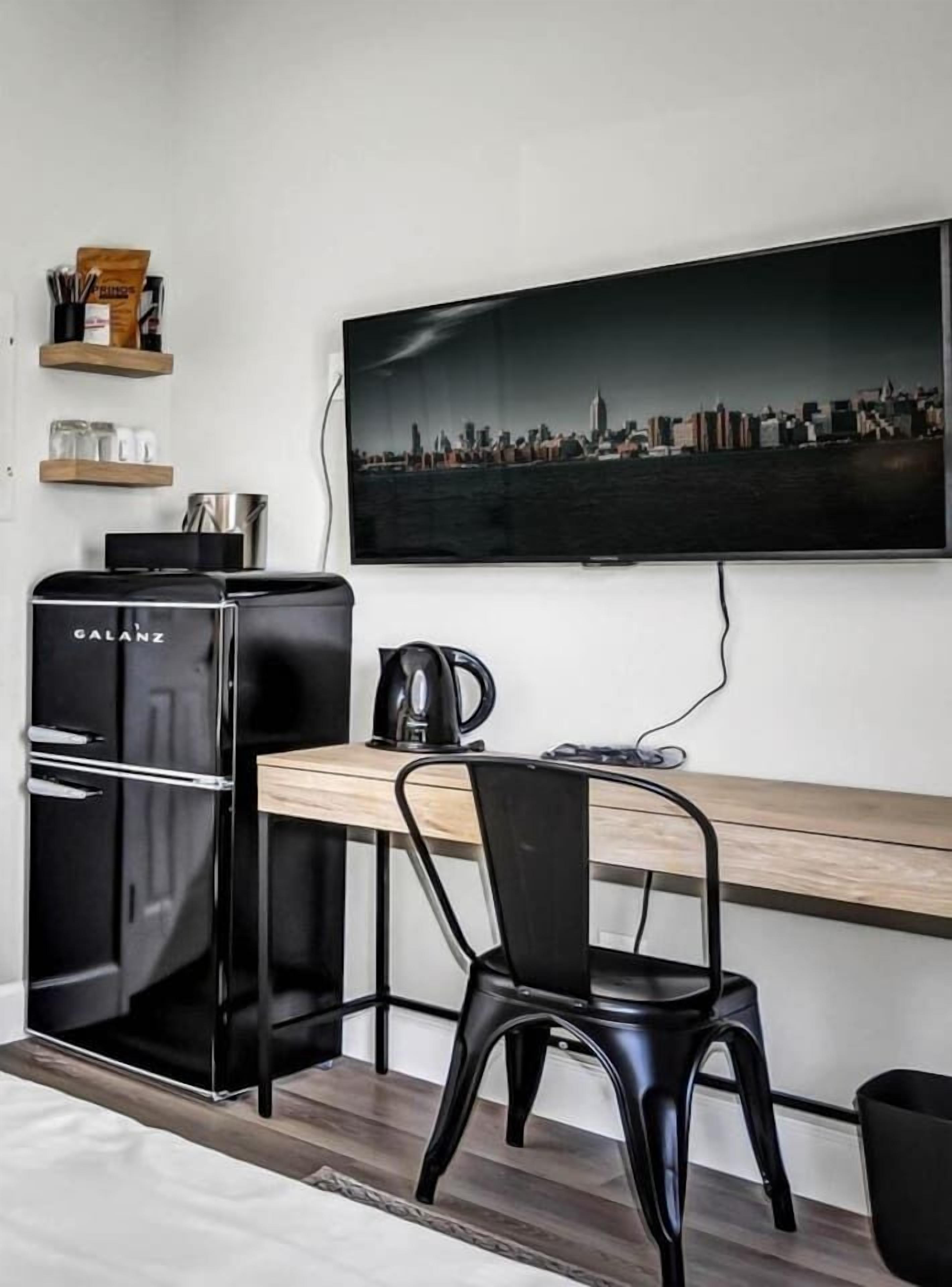 A compact kitchenette with a Galanz refrigerator, a coffee maker, and a flat-screen TV mounted on the wall.