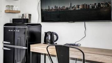 A compact kitchenette with a Galanz refrigerator, a coffee maker, and a flat-screen TV mounted on the wall.