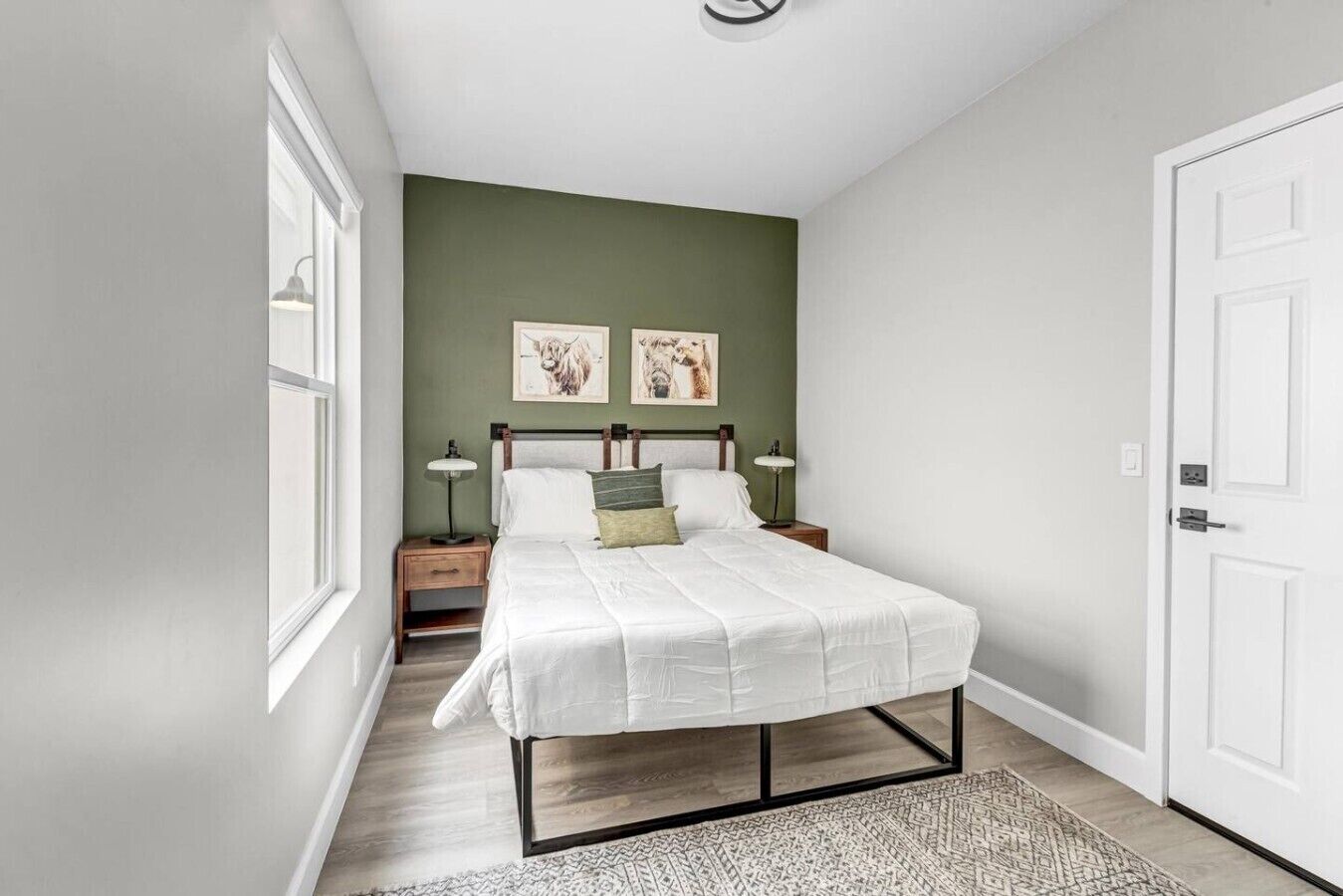 A bedroom with a bed, two bedside tables, a window, and two wall-mounted pictures.