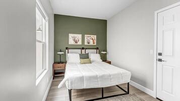 A bedroom with a bed, two bedside tables, a window, and two wall-mounted pictures.