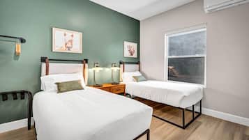 A bedroom with two beds, a window, and artwork on the walls.