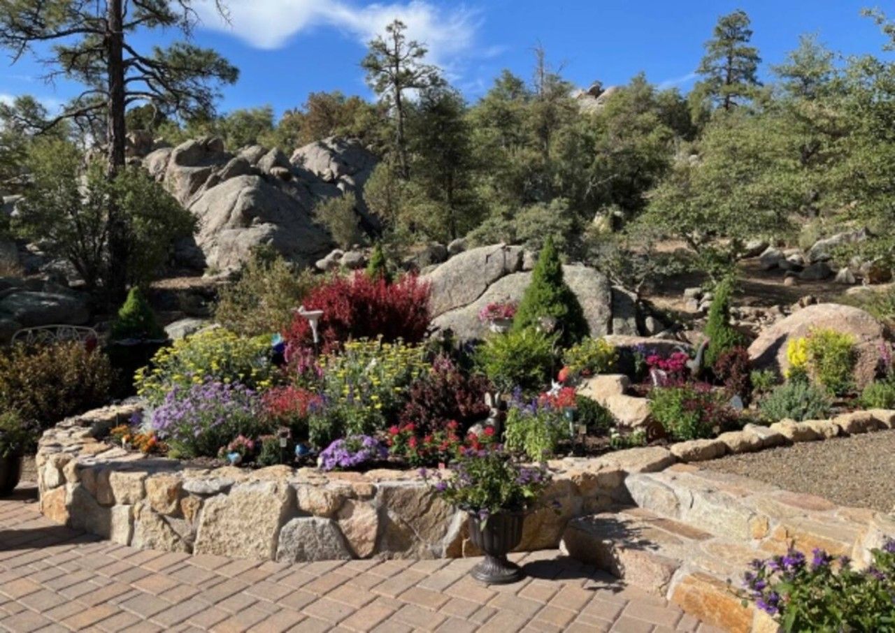A landscaped garden with a variety of plants and flowers, a stone retaining wall, and a rocky hillside in the background.