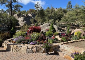 A landscaped garden with a variety of plants and flowers, a stone retaining wall, and a rocky hillside in the background.