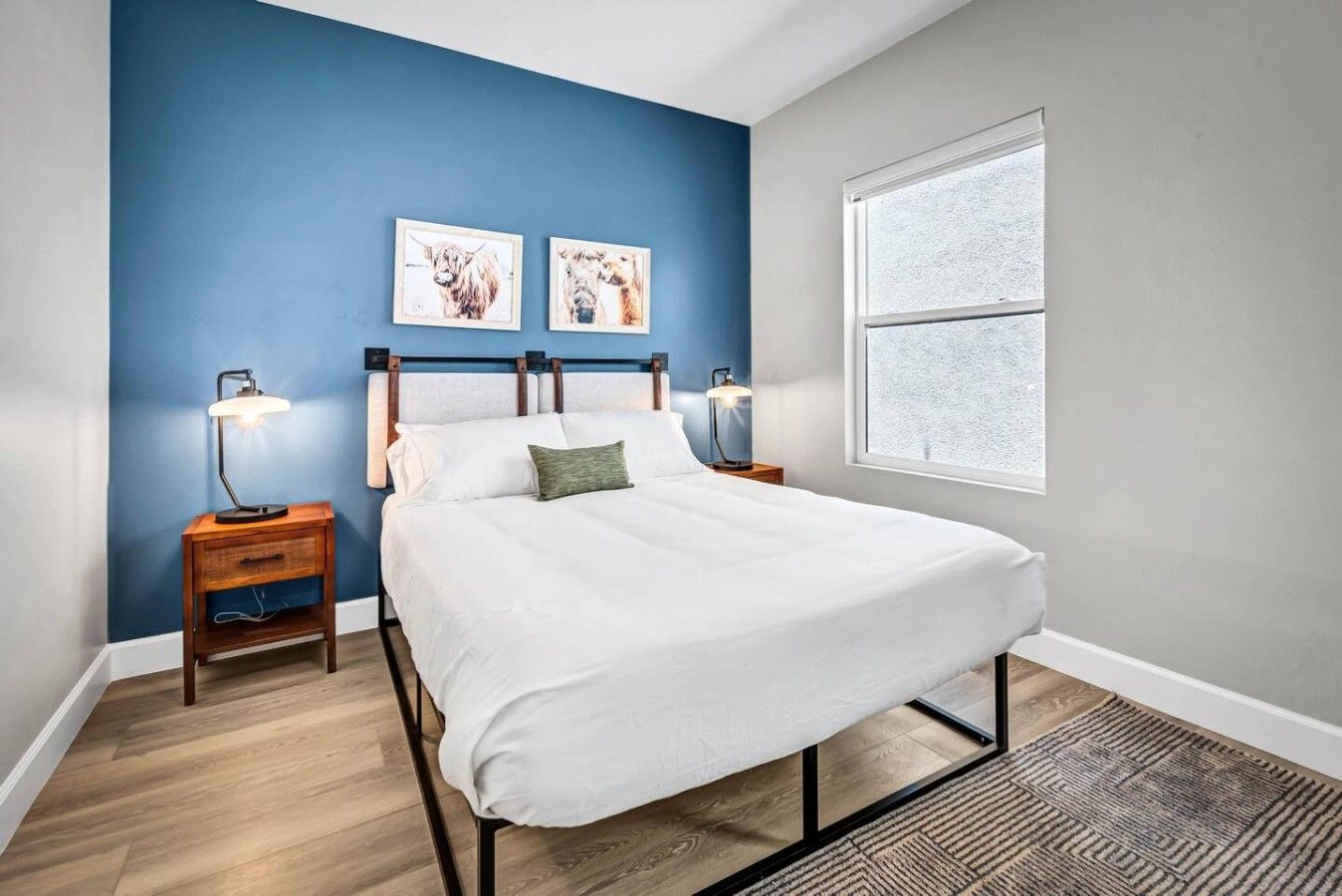 A bedroom with a bed, two bedside tables, a window, and two wall-mounted pictures.