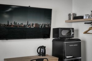 Une chambre moderne équipée d’un téléviseur diffusant des images de la ville, d’un réfrigérateur Galanz noir et d’une table en bois.