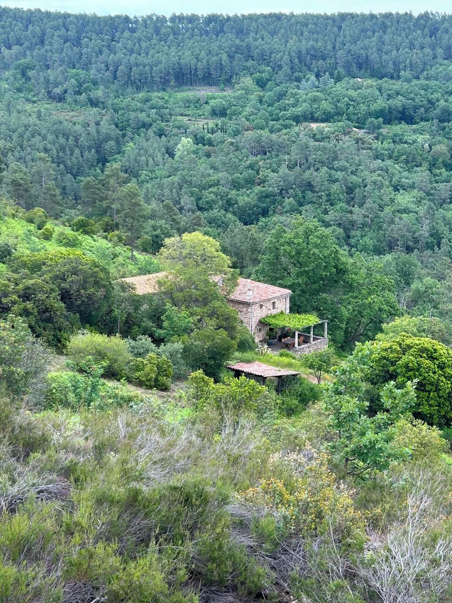 A rustic stone building with a red-tiled roof, surrounded by dense forest.