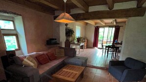 Un vaste espace de vie comprenant un canapé, des fauteuils, une table basse et une table à manger. On y trouve également un ventilateur de plafond et un luminaire suspendu.