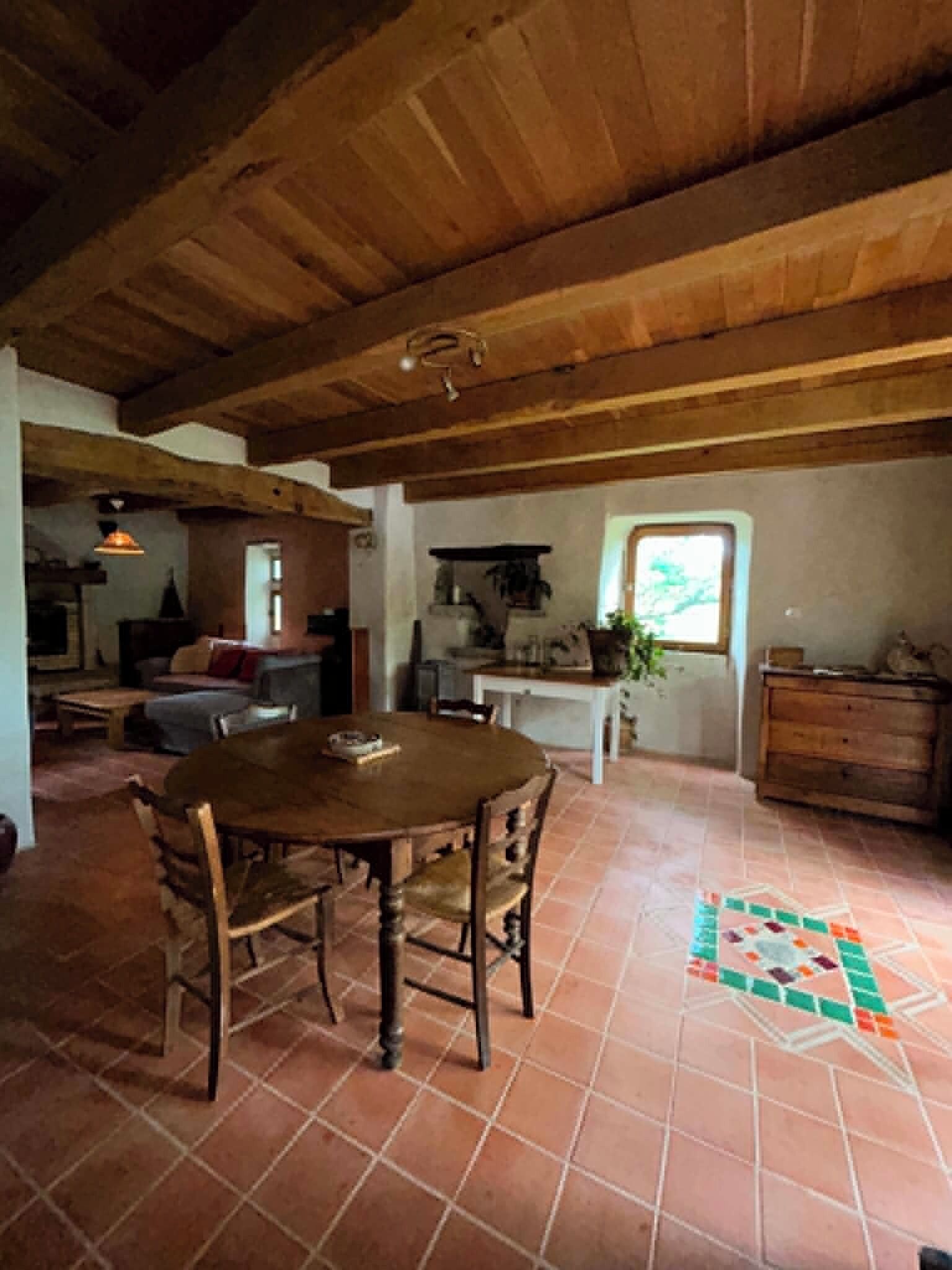 A rustic interior with a wooden dining table, chairs, a tiled floor, and a window with a view.