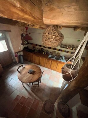 Eine rustikale Küche mit Holztisch, an der Decke befestigten Kochtöpfen und einer gefliesten Spritzschutzeinrichtung.