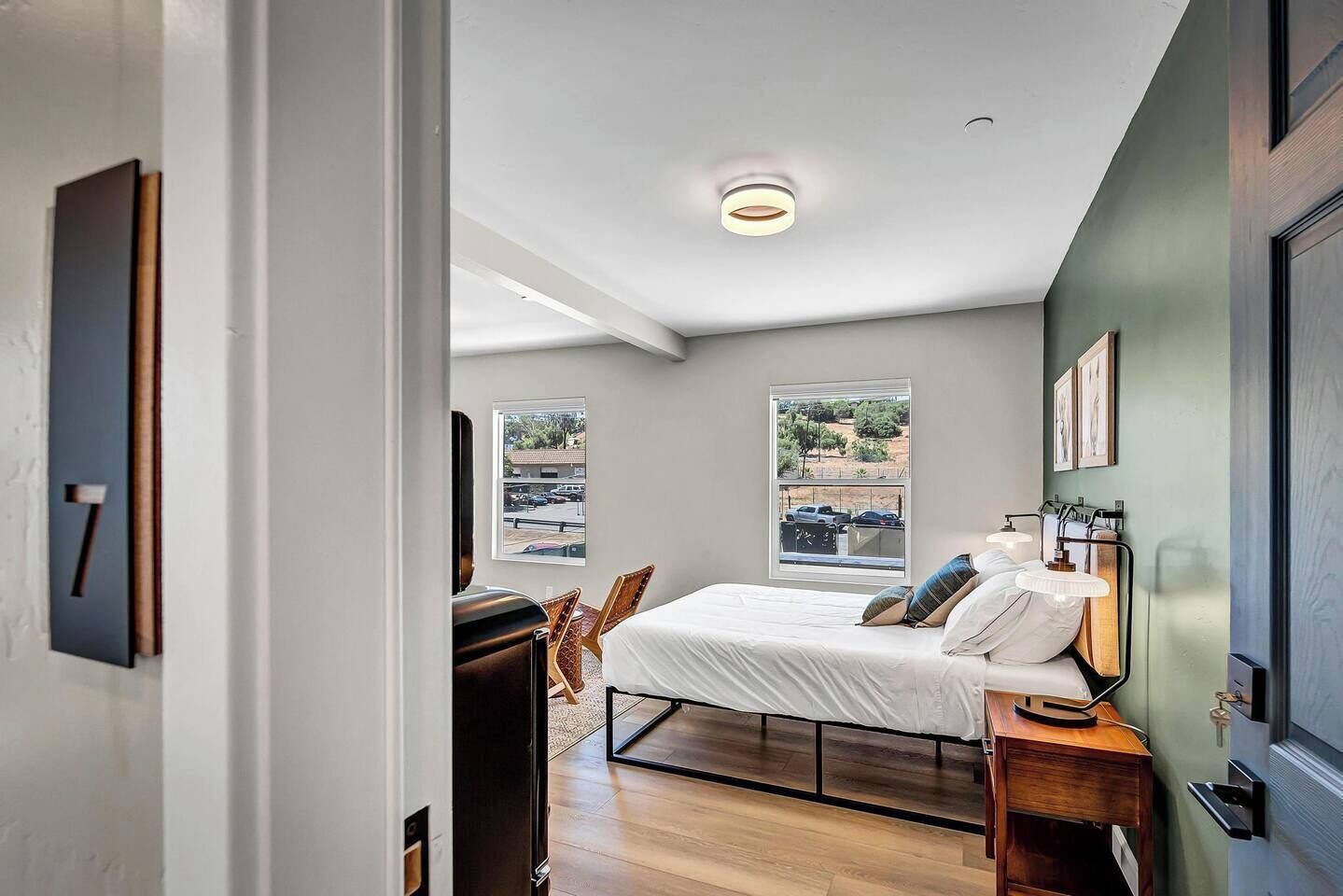 A bedroom with a bed, bedside table, lamp, and a view of the outside.