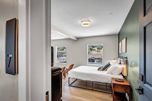 Un dormitorio con cama, mesita de noche, lámpara y vistas al exterior.