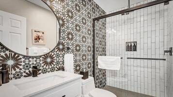 A bathroom with a white sink, a toilet, a shower with a glass door, and a patterned wall.