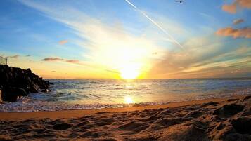 A beach with a sunset, waves, and a jet trail.