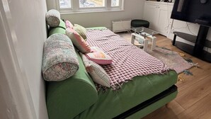 A bedroom with a green sofa bed, a window with a view of buildings, a radiator, a TV, and a wall-mounted deer head decoration. - Western 3 bedroom en-suite maisonette (Saint Leonards)