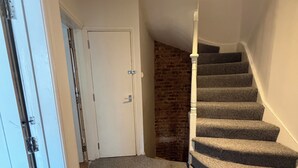 A carpeted staircase with a brick wall and a white door. - Western 3 bedroom en-suite maisonette (Saint Leonards)