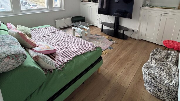 A room with a green sofa, a television, a small desk, and a window with a view of buildings outside. - Western 3 bedroom en-suite maisonette (Saint Leonards)