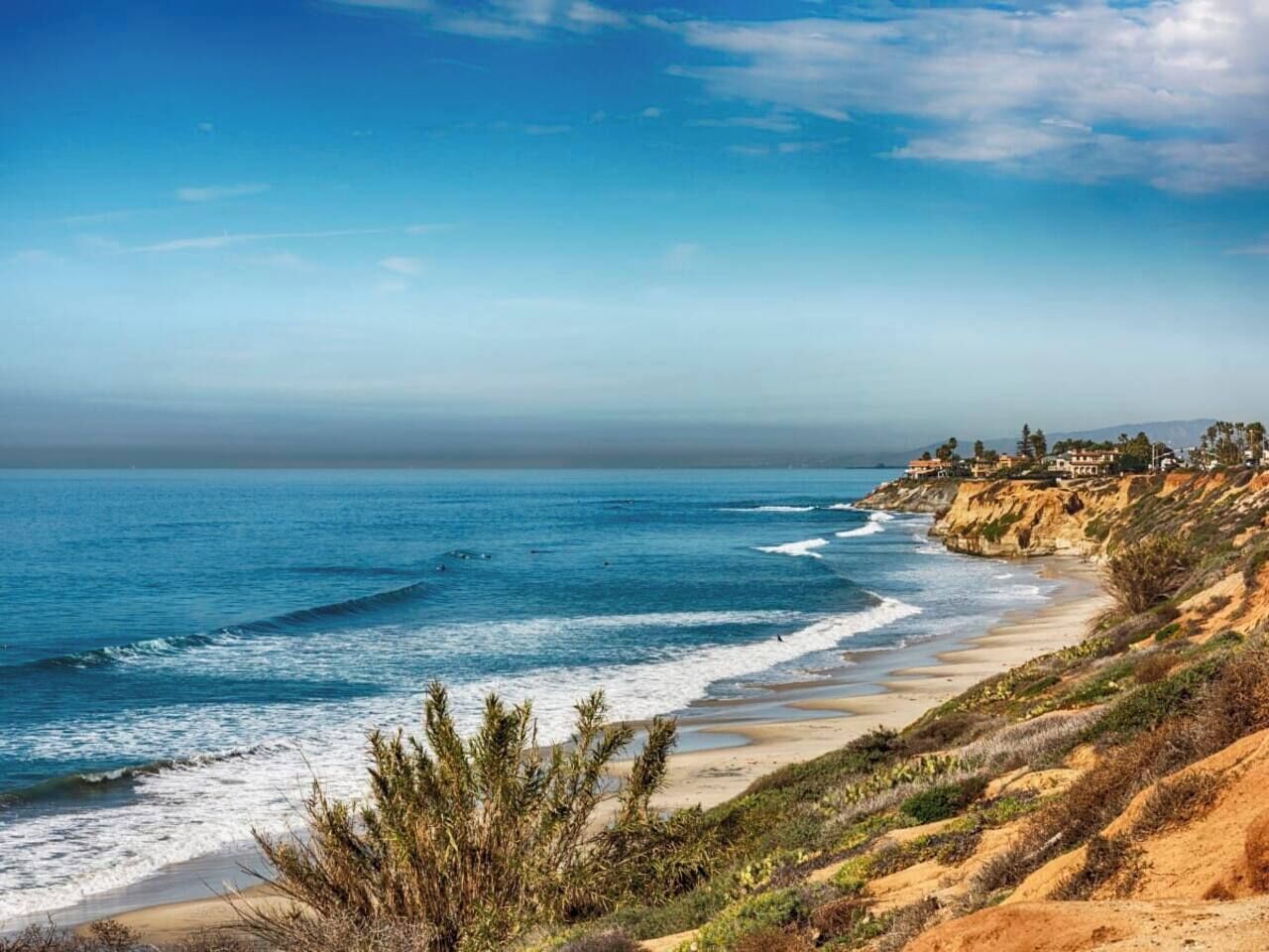 Un paisaje costero con playa, olas del océano y un acantilado con casas.