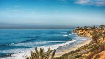 Un paisaje costero con playa, olas del océano y un acantilado con casas.