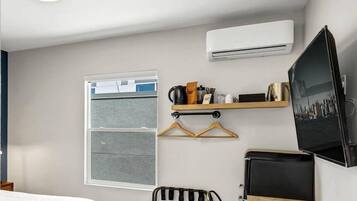 A compact room with a bed, a small table, a chair, a TV, and an air conditioning unit.