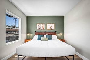 A bedroom with a large bed, two bedside lamps, a headboard, and two framed pictures on the wall. - Chic Studio in Historic City Center, Near Carlsbad (Vista)