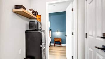 A hallway with a black refrigerator, a wooden shelf, and a trash bin.