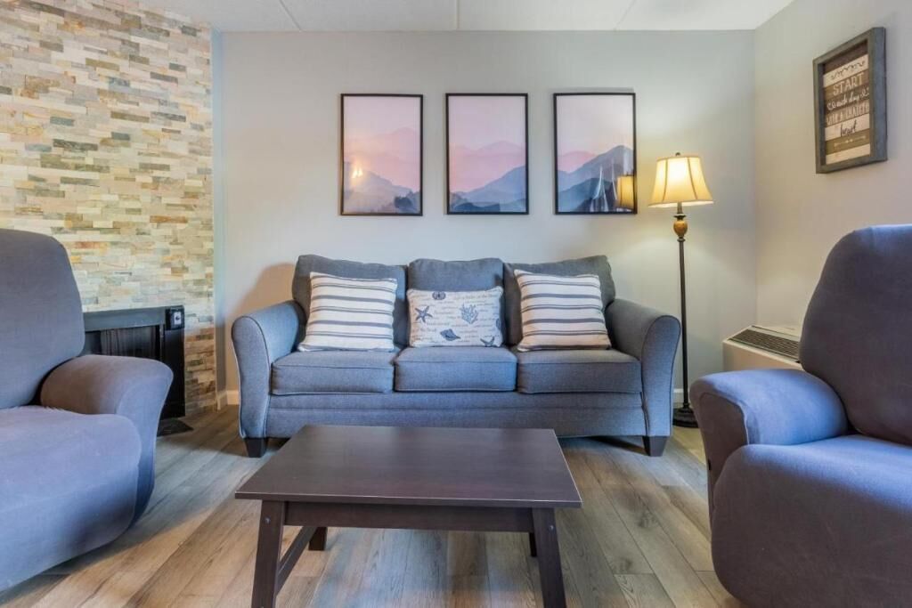A living room with a grey sofa, two armchairs, a coffee table, and a wall-mounted lamp.