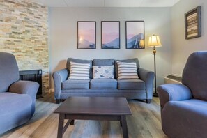 Una sala de estar con un sofá gris, dos sillones, una mesa de centro y una lámpara de pared.