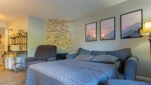 A bedroom with a bed, two armchairs, a small table, and a wall-mounted shelf. - OLDE GATLINBURG RANTEL (Gatlinburg)