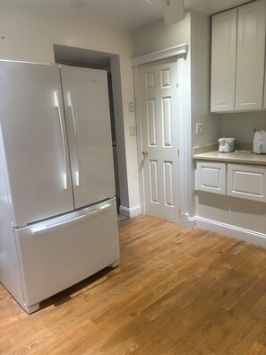 Eine Küche mit einem weißen Kühlschrank, Holzboden und weißen Schränken.