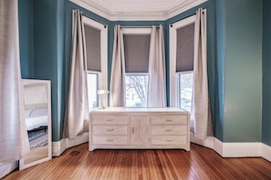 Una habitación con paredes color turquesa, piso de madera, cómoda blanca y ventana con persianas.