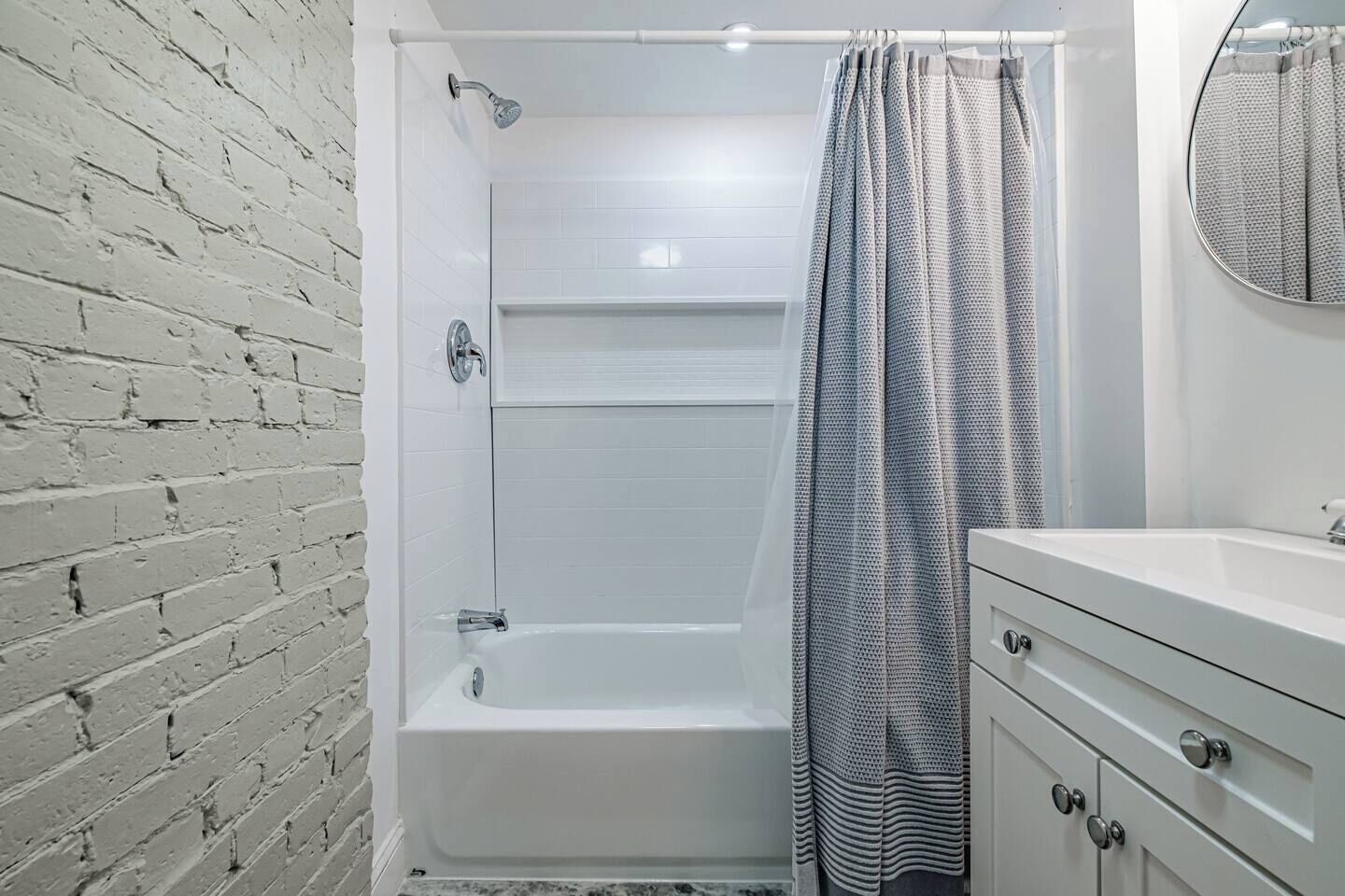 A bathroom with a white bathtub, a shower, a white vanity with drawers, and a mirror.