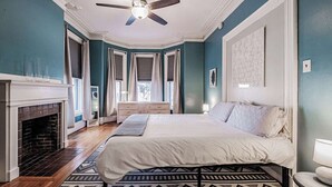 A bedroom with a bed, a fireplace, a ceiling fan, and a patterned rug. - Experience Portland’s charm in this beautifully restored 2-bed, 1.5-bath Victorian apartment! Located downtown, enjoy modern comforts, historic elegance, a private backyard, AC, and 1 free parking spot. Perfect for your Maine getaway! 🦞 (Portland)